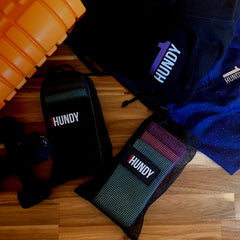 Three resistance bands laid out on the floor with a black, grey, and blue pattern. The brand 1Hundy is visible on the bands.